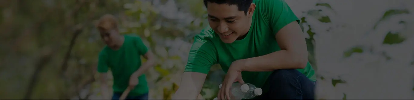 Imagem de um homem sorrindo, mexendo em plantas e segurando duas garrafas pets. Ao fundo um outro homem preparando a terra para o plantio.
